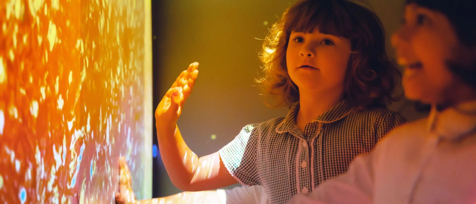 Two children in a room with an interactive wall, one reaching out to touch it.