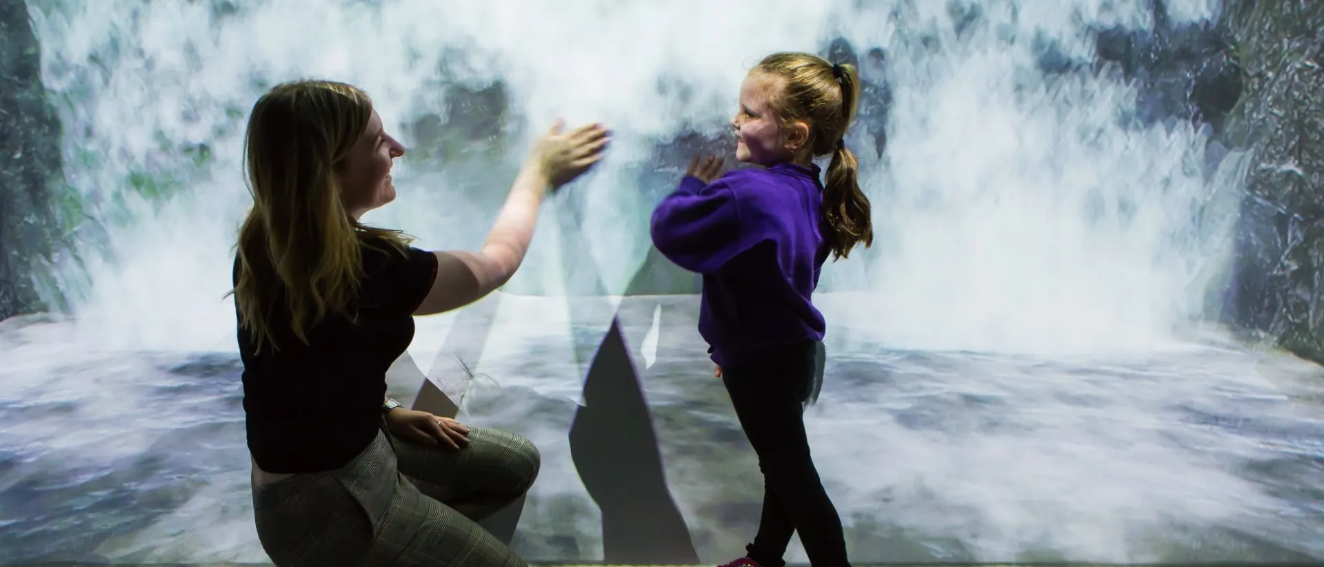 A woman on the left and a child on the right touching the wall of an interactive room
