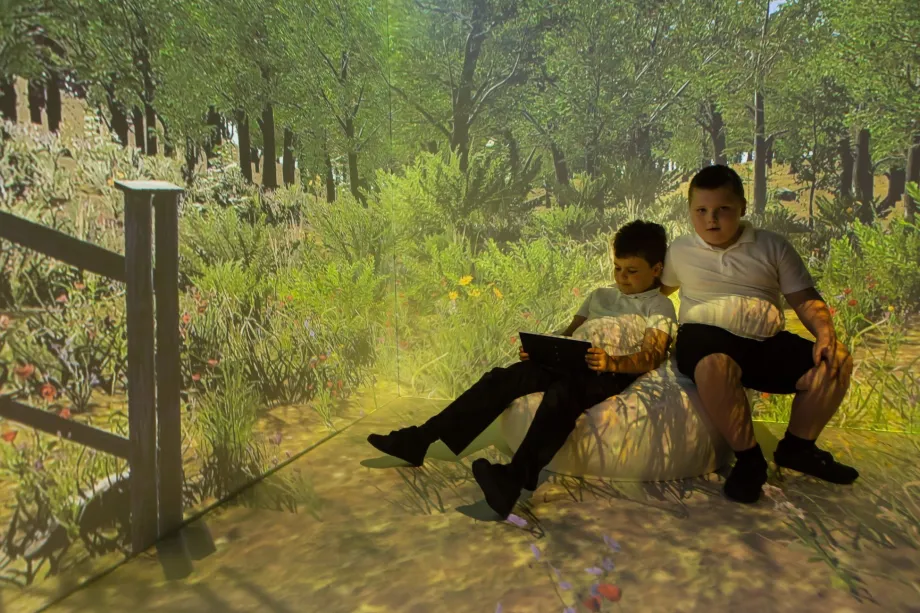 Two children sat down in an interactive room, one on the left with a laptop